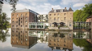 Un bâtiment historique doté d’une extension moderne en verre, qui se reflète dans une étendue d’eau paisible.
