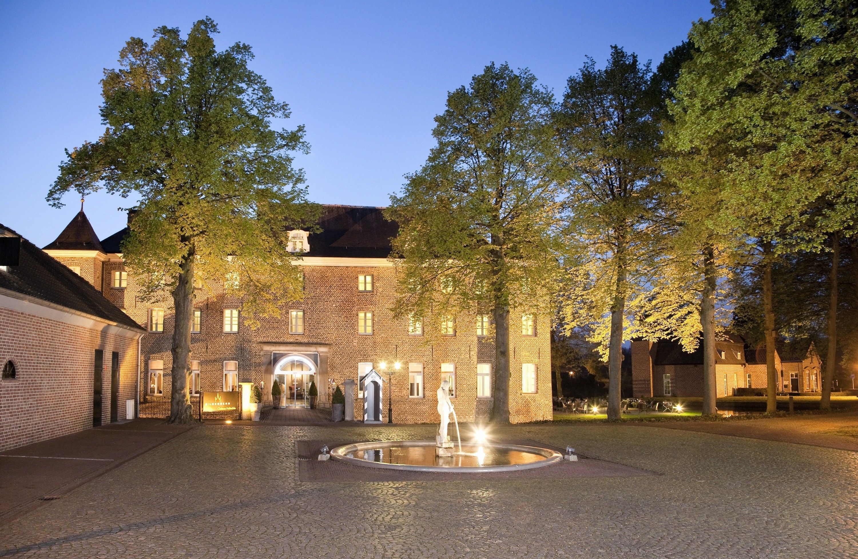 A courtyard with a fountain, brick buildings, and trees.