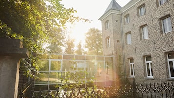 A brick building with a tower, a metal fence, and a tree in the foreground.