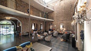 Un vestíbulo amplio con techo alto, paredes de ladrillo visto y un nivel intermedio. Hay varias zonas de estar con muebles modernos y un candelabro.