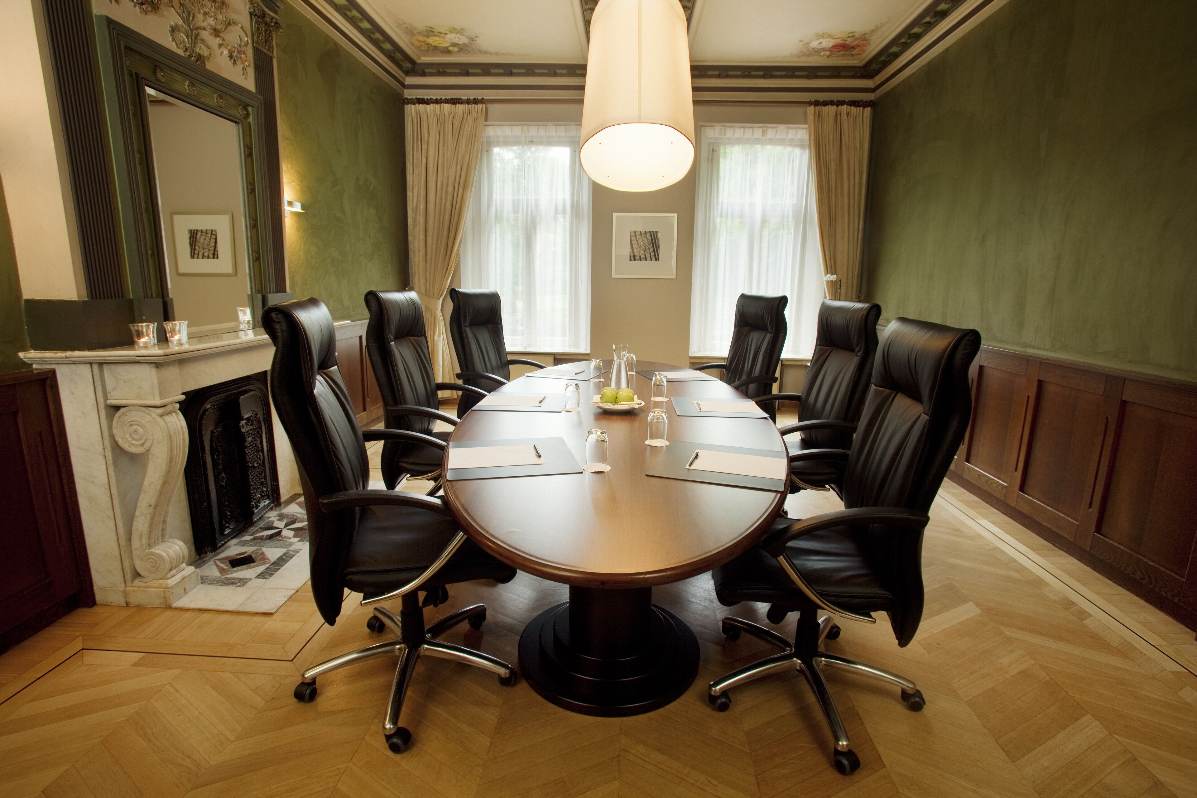 A conference room with a round table, eight leather chairs, a fireplace, and a large mirror.