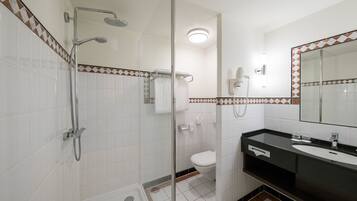 Une salle de bain moderne avec une douche à parois de verre, des toilettes blanches et un lavabo noir avec un miroir au-dessus.
