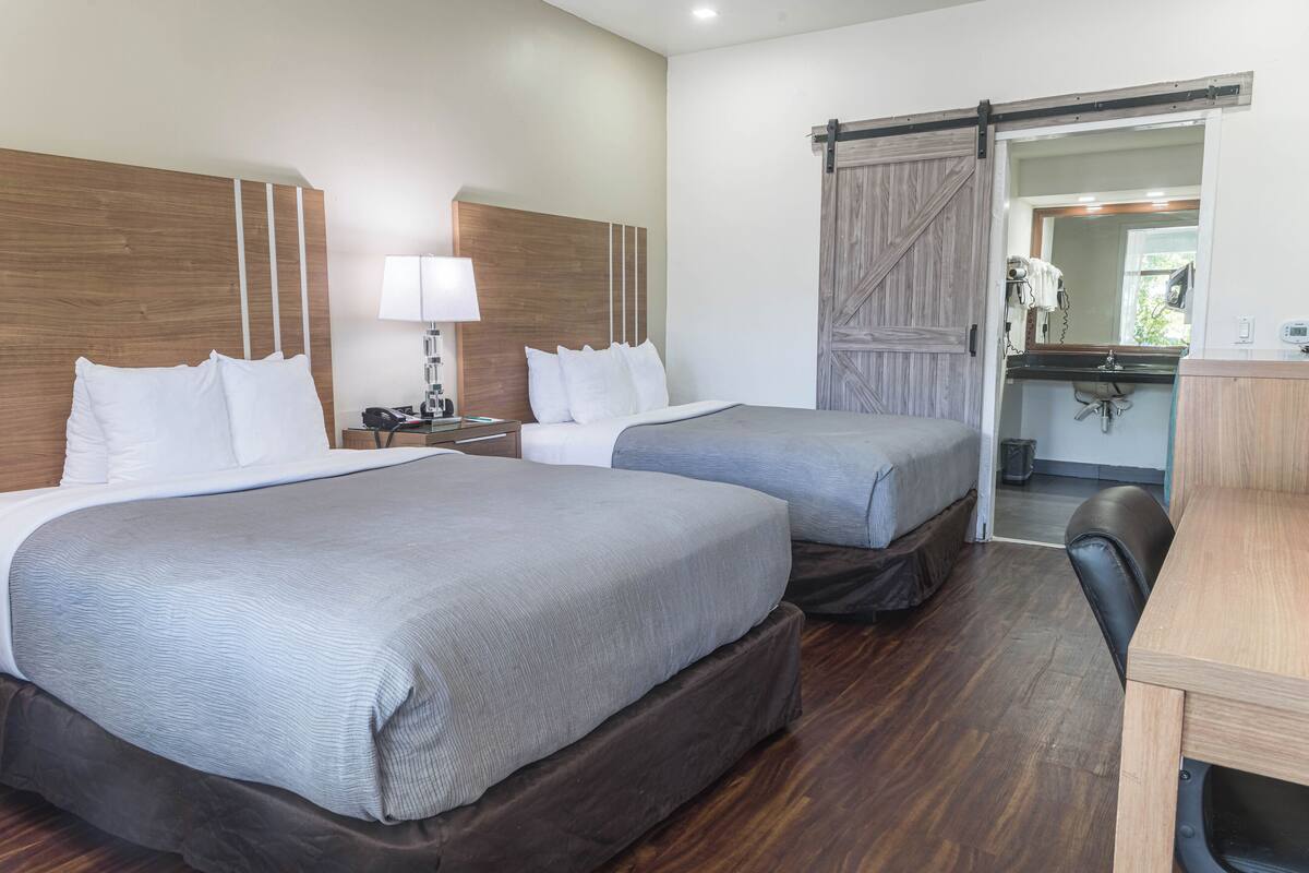 A hotel room with two beds, a desk, a chair, a large mirror, and a sliding door to the bathroom.