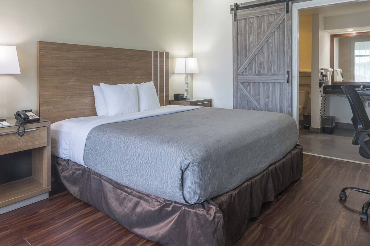 A neatly made bed with a wooden headboard, a bedside lamp, and a telephone on a wooden nightstand.