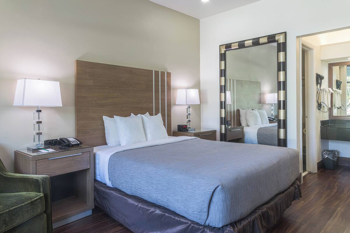 A hotel room with a large bed, two bedside tables with lamps, a mirror, and a green chair.