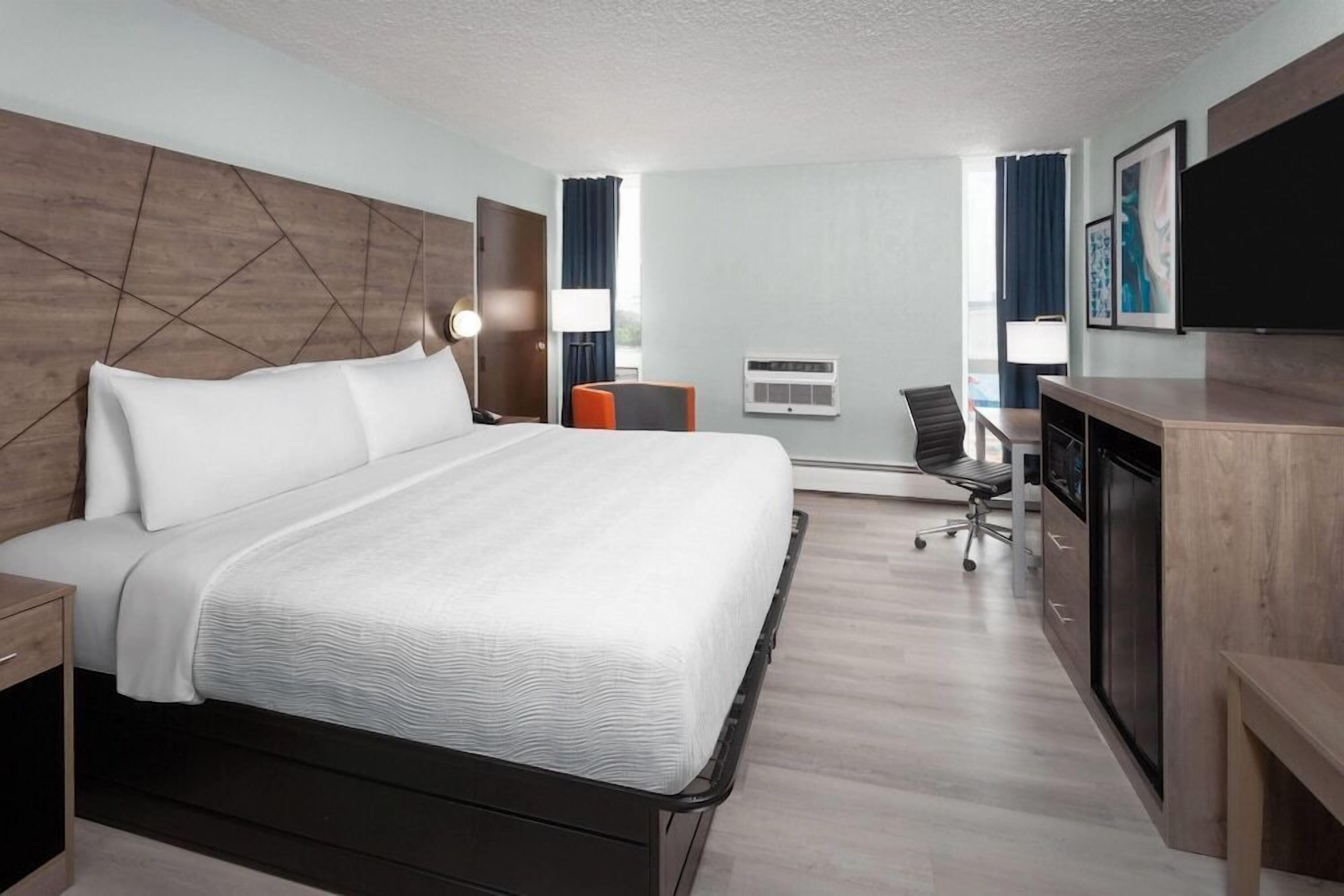 A hotel room with a large bed, a desk with a chair, a flat-screen TV, and a window with curtains.