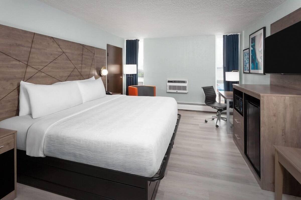 A hotel room with a large bed, a desk with a chair, a flat-screen TV, and a window with curtains.