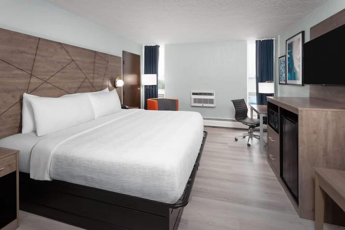 A hotel room with a large bed, a desk with a chair, a flat-screen TV, and a window with curtains.