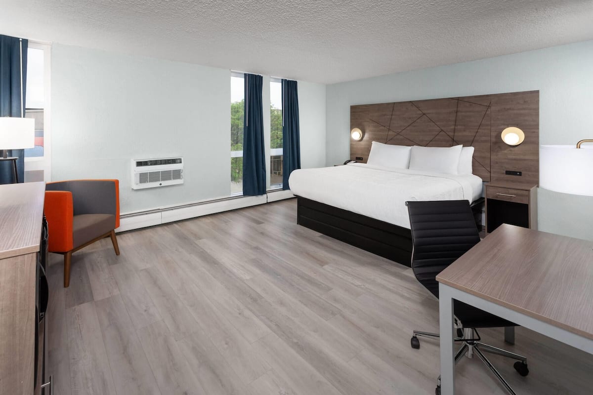 A modern hotel room with a large bed, a desk, a chair, and a view of the outdoors.