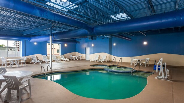Piscina interna com espreguiçadeiras e mesas, água azul cristalina e teto alto com vigas aparentes.