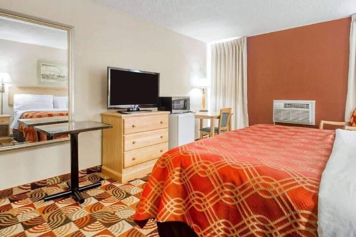 A hotel room with a bed, a TV, a desk, a dresser, and a mirror.