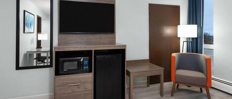 Habitación de hotel con televisor de pantalla plana, mini refrigerador, microondas, escritorio de madera, una silla y un ventanal con cortinas.
