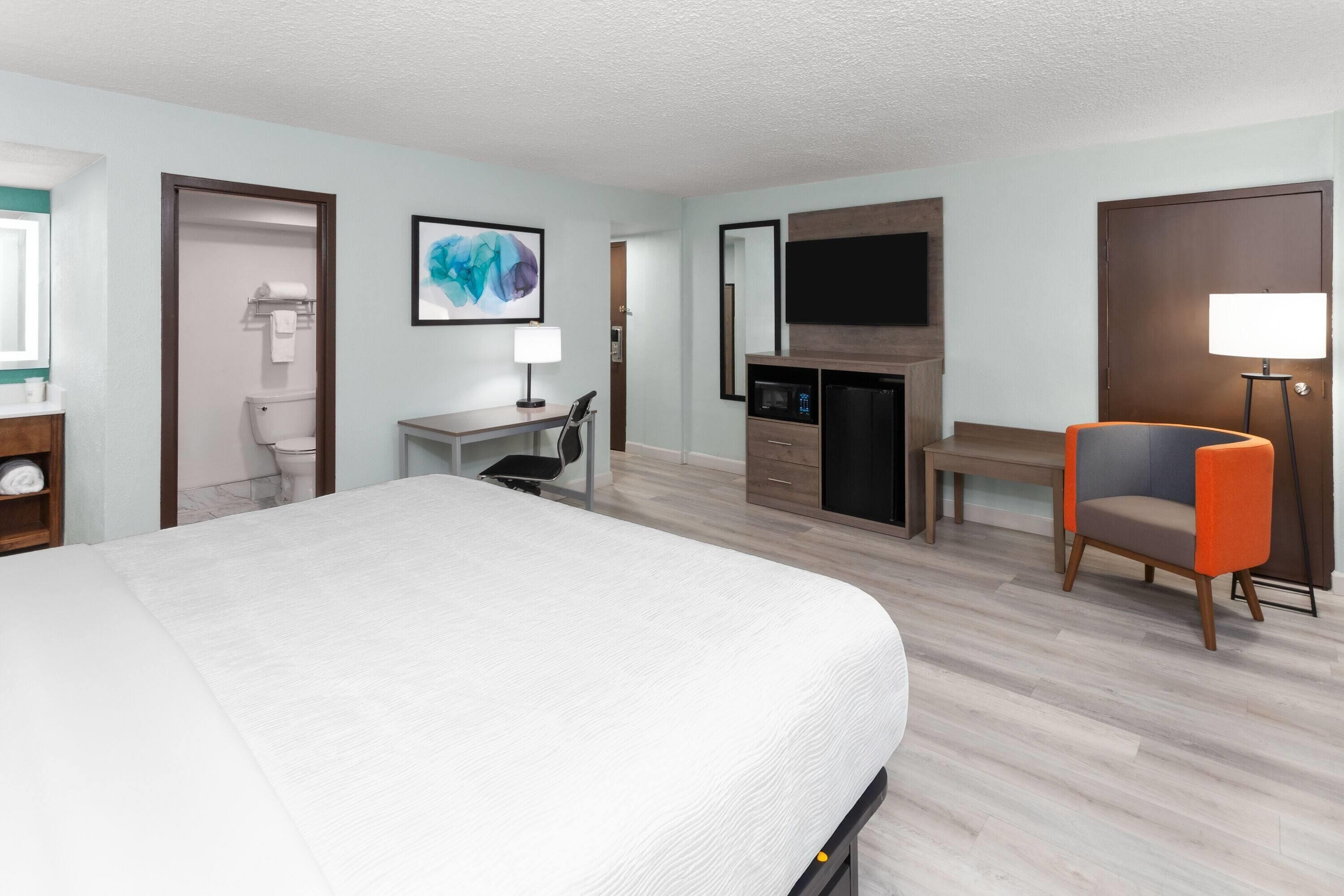A hotel room with a bed, desk, chair, TV, and a fireplace.
