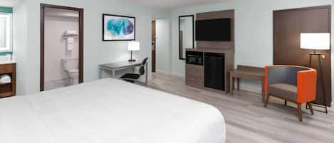 A hotel room with a bed, desk, chair, TV, and a fireplace.