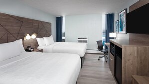 Quarto de hotel com duas camas, uma escrivaninha, uma cadeira, uma televisão e um ar condicionado.