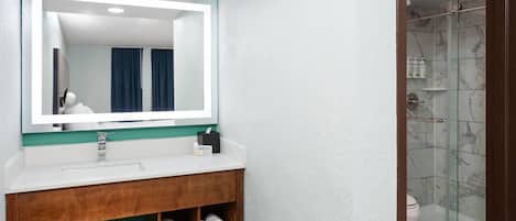 A bathroom with a mirror, sink, and shower.