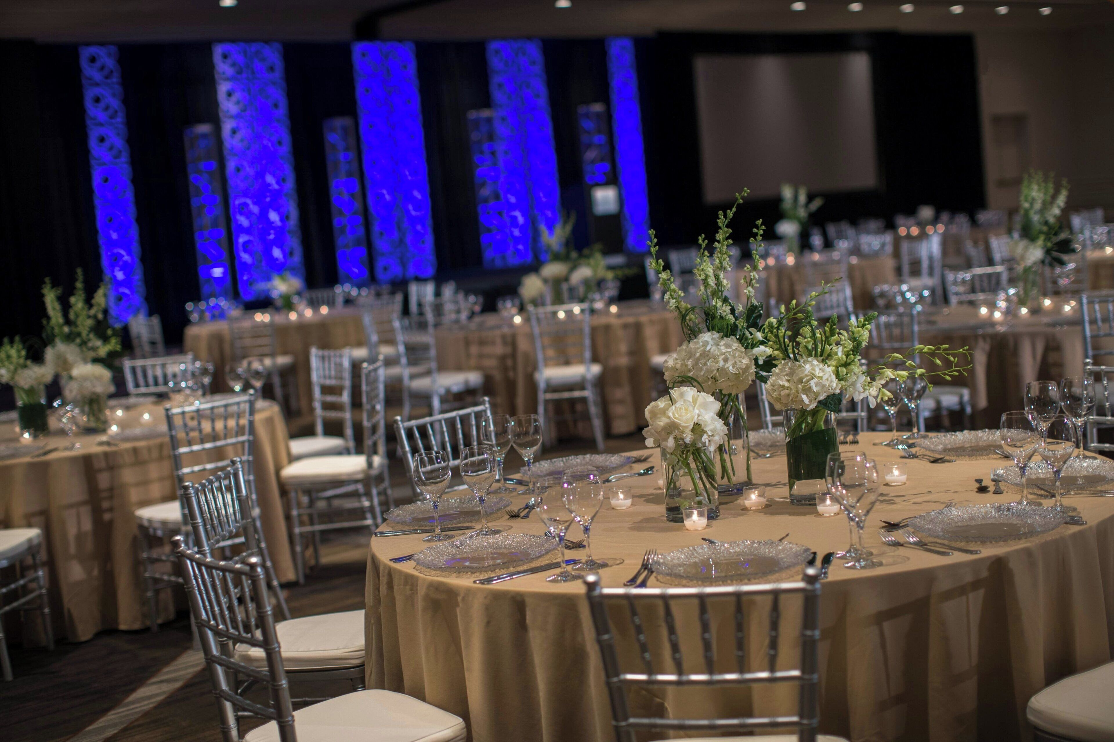 A banquet hall with round tables set for a formal event, featuring floral centerpieces and elegant table settings.