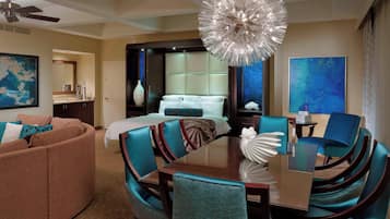 A hotel room with a bed, a dining table with chairs, a sofa, a chandelier, and artwork on the walls.