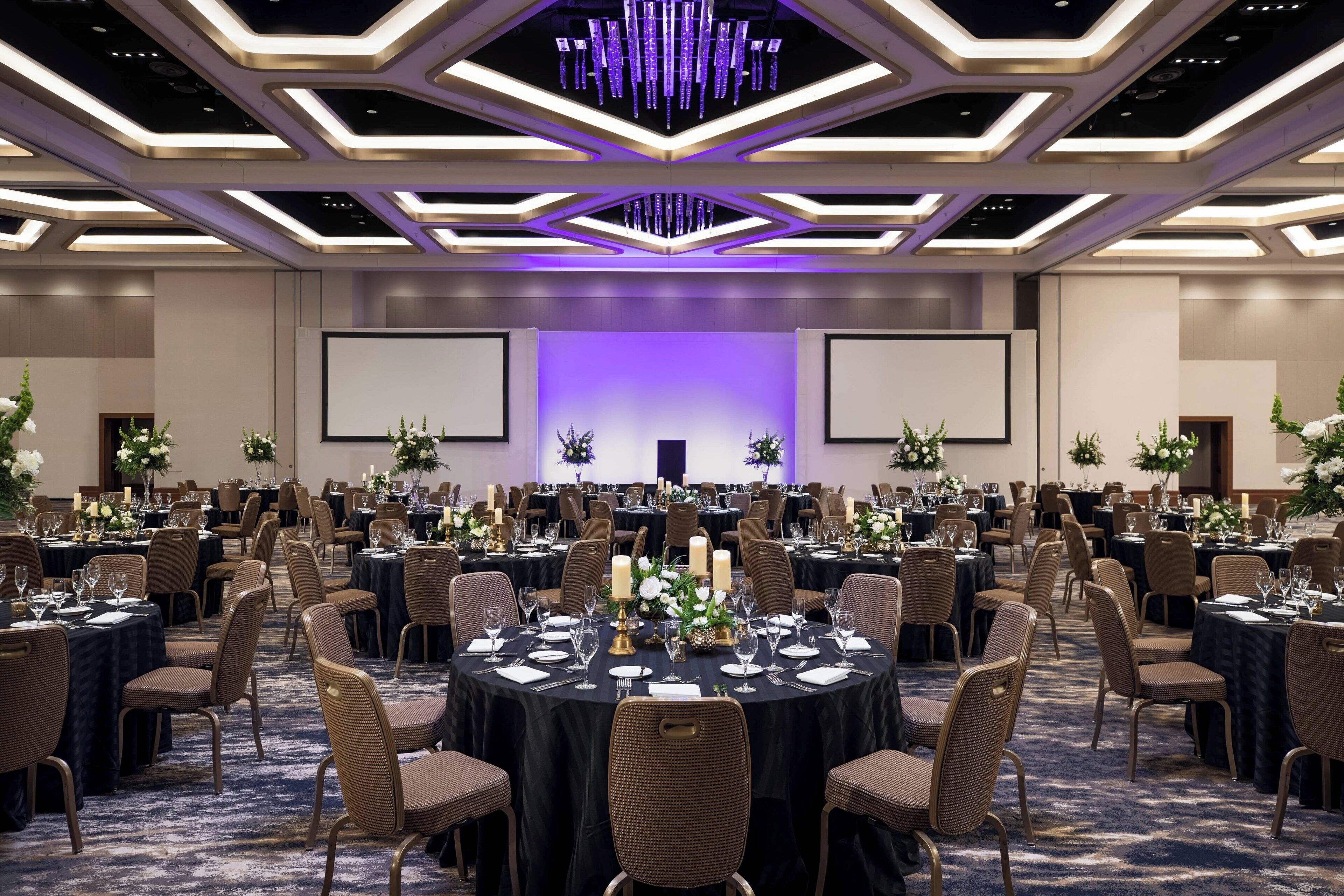 Un gran salón de banquetes con mesas redondas, sillas y centros de mesa florales.