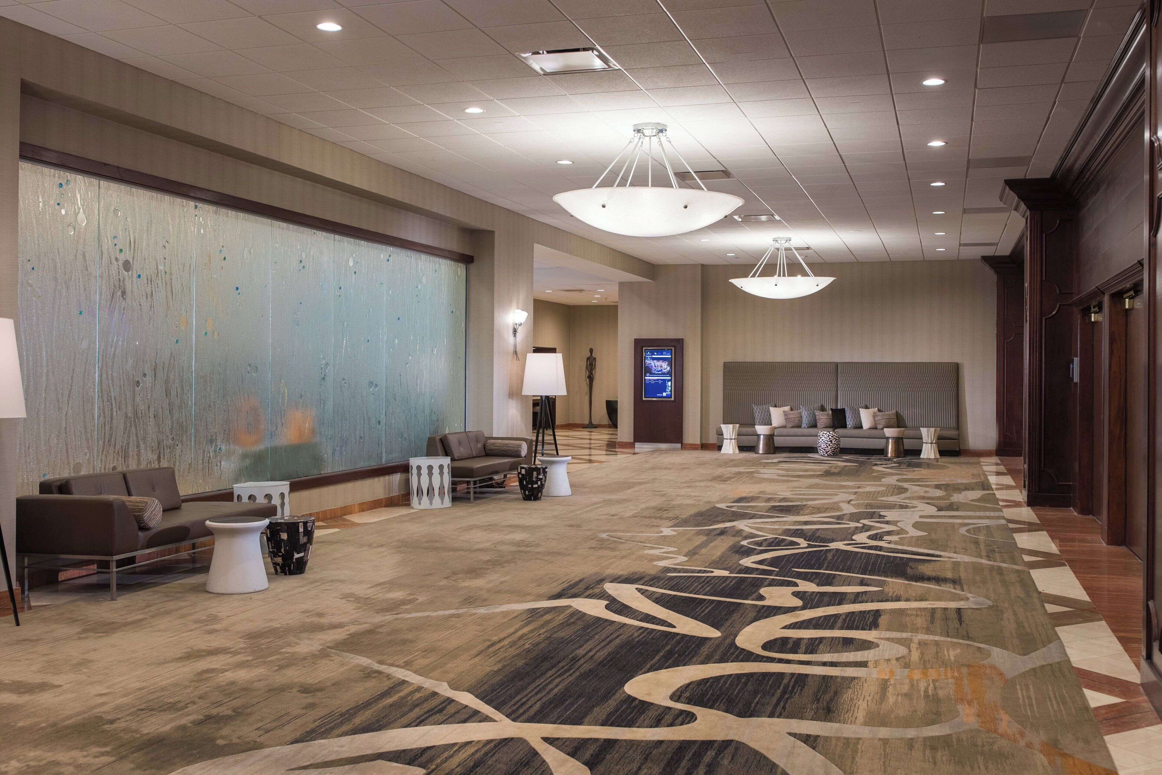 A spacious lobby with a large abstract wall, a reception desk, seating area, and a patterned carpet.