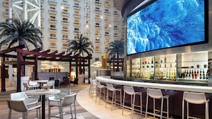 A bar area with a large screen displaying a blue abstract image, surrounded by bar stools and a seating area with chairs and a round table. - Renaissance Orlando at SeaWorld (Orlando)