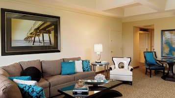 A living room with a brown sofa, teal pillows, a coffee table with books, a lamp, and a framed picture of a pier.