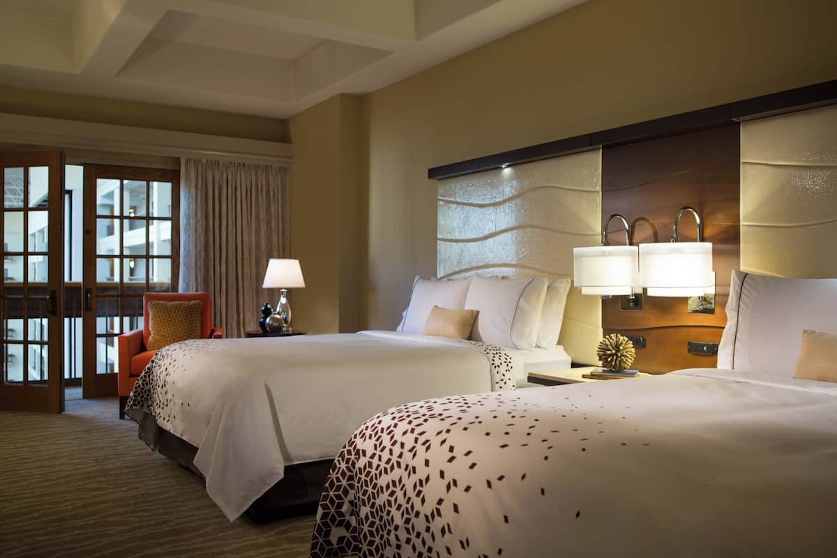 Een hotelkamer met twee bedden, een zithoek met een stoel, een lamp en een decoratief wandobject.