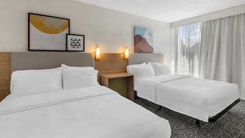 A hotel room with two beds, a nightstand, wall-mounted lamps, and artwork.