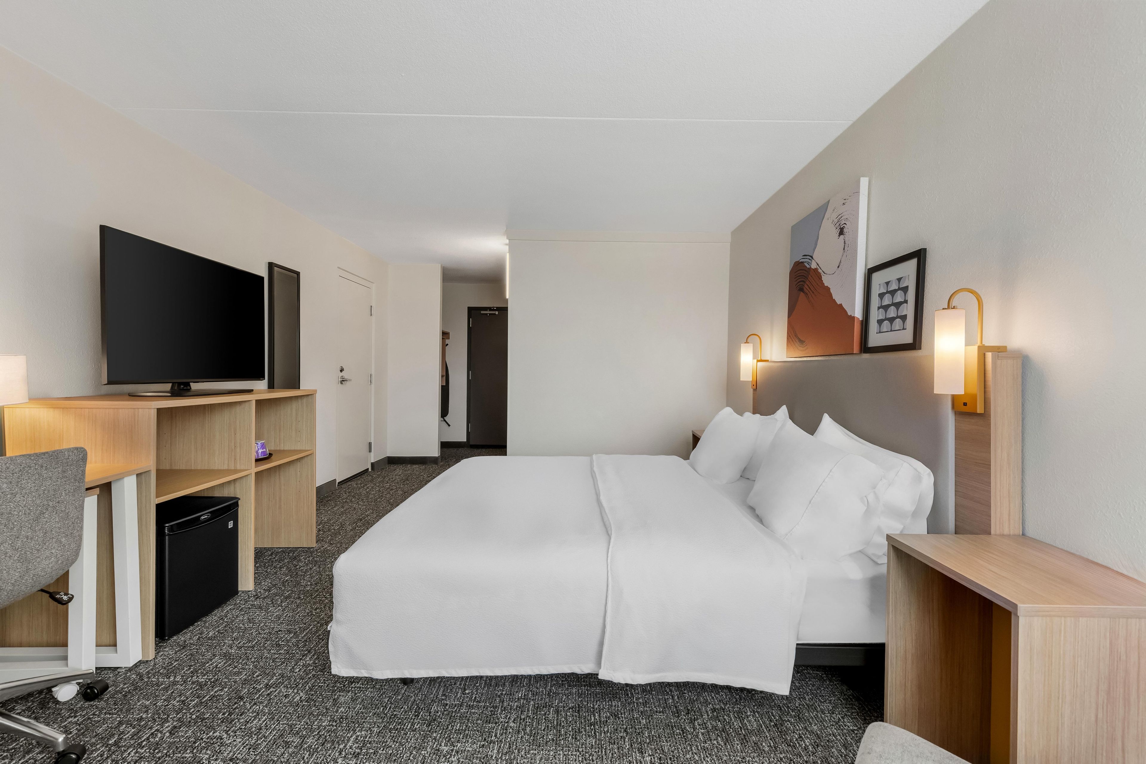 Een hotelkamer met een bed, een bureau met een computer, een televisie en een badkamer die door een open deur zichtbaar is.