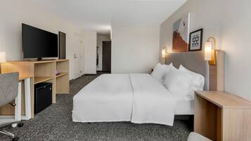 Een hotelkamer met een bed, een bureau met een computer, een televisie en een badkamer die door een open deur zichtbaar is.