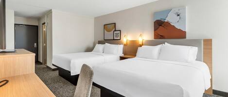 A hotel room with two beds, a desk, and a TV.