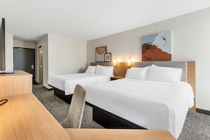 A hotel room with two beds, a desk, and a TV.