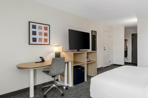 Quarto de hotel com escrivaninha, cadeira, televisão e cama.