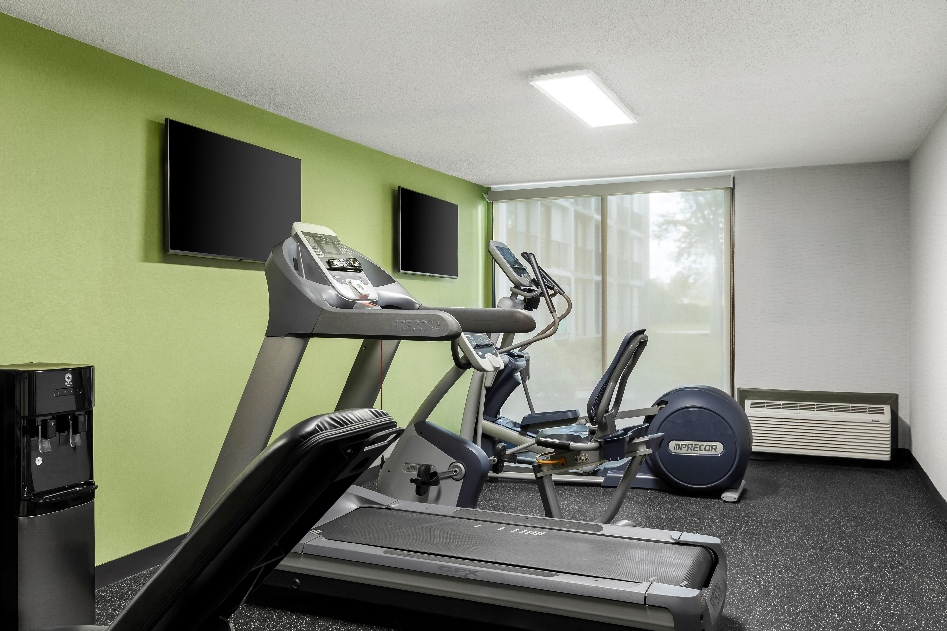 Un gimnasio con cintas de correr, elíptica y dispensador de agua.