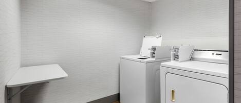 A laundry room with two washing machines, a drying rack, and a wooden floor.