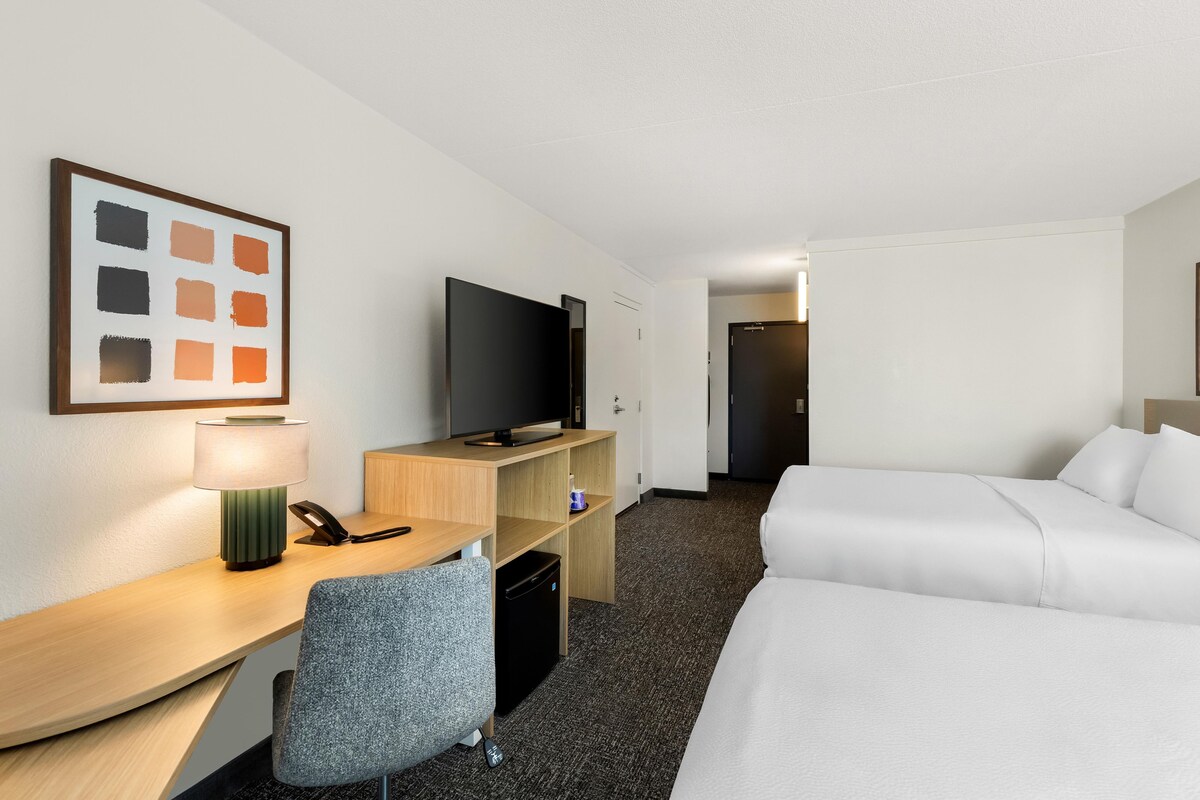 A hotel room with a desk, a television, a bed, and a chair.