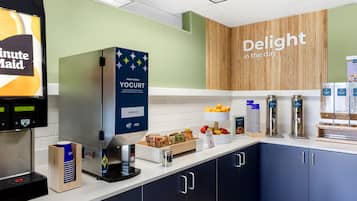 Een ontbijtbuffet met een yoghurtautomaat, een koffieapparaat en diverse soorten eten.