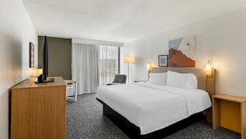 A hotel room with a bed, bedside tables, a desk, a chair, and a window with curtains.
