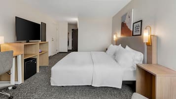 Habitación de hotel con cama, escritorio con computadora, televisión y baño visible a través de una puerta abierta.