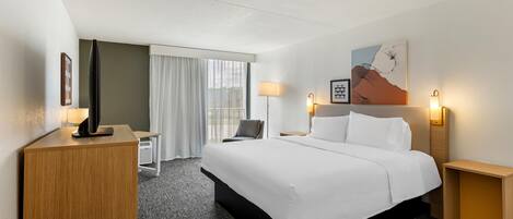 Une chambre d’hôtel avec un lit, des tables de chevet, un bureau, une chaise et une fenêtre avec des rideaux.