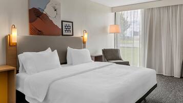 A hotel room with a large bed, two bedside lamps, a chair, and a window with curtains.