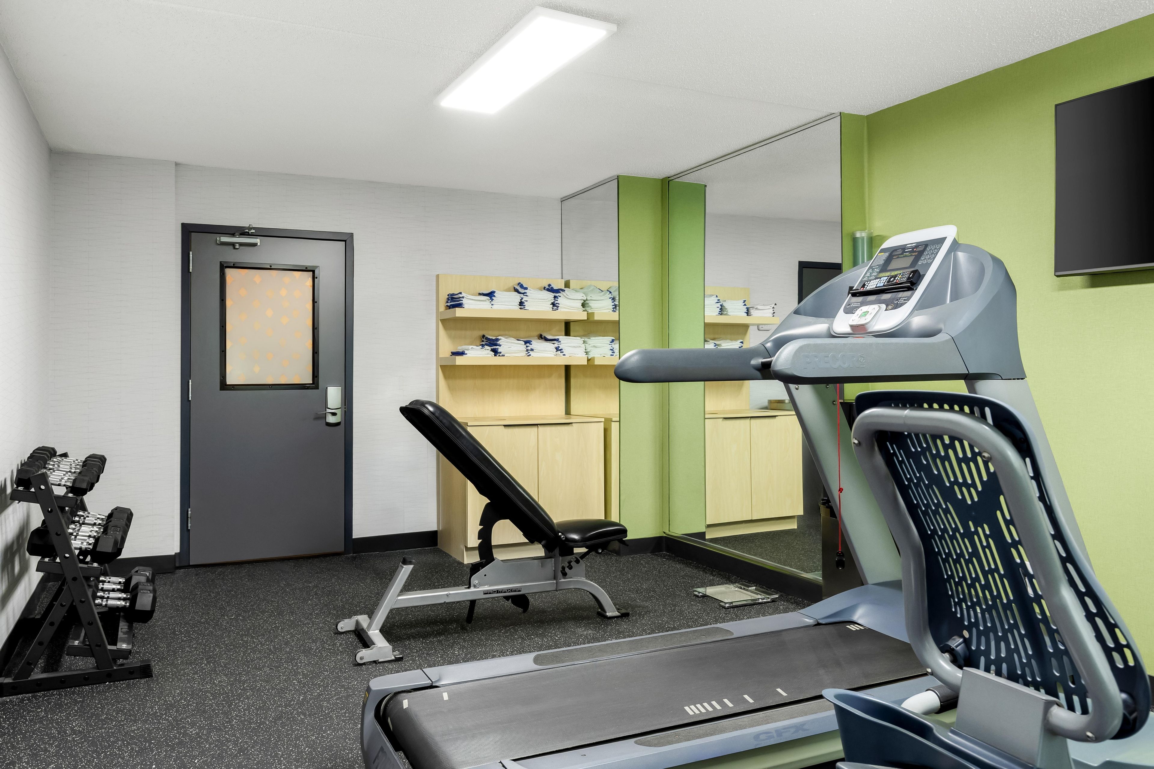 A gym with exercise equipment, a treadmill, and a wall-mounted TV.