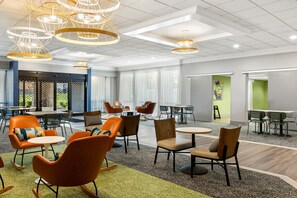 A modern hotel lobby with multiple seating areas, including orange chairs and tables, and a large window providing a view of the outdoors. - Spark by Hilton Akron Fairlawn (Akron)