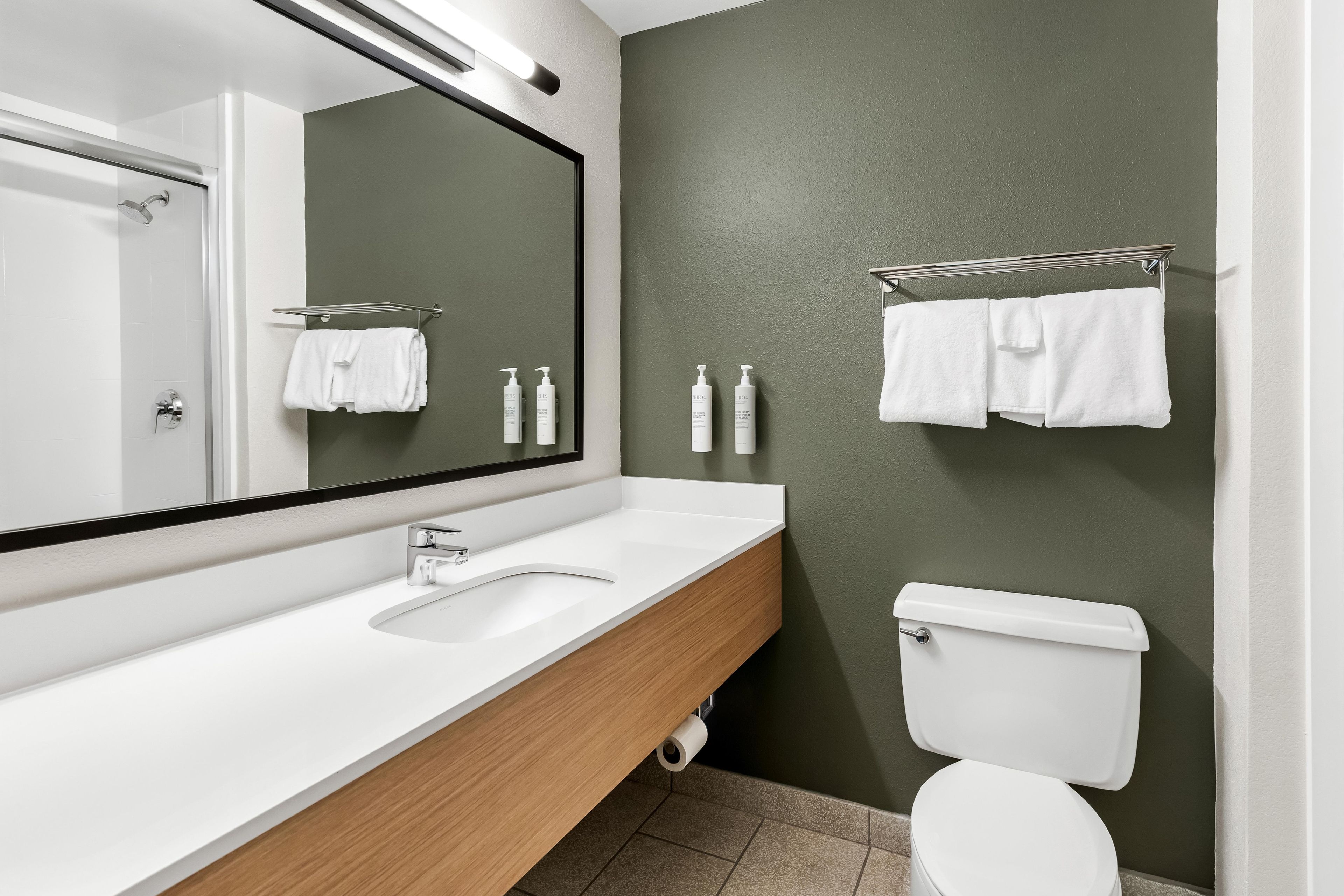 Un baño moderno con un lavamanos blanco, un espejo, un inodoro y un perchero para toallas.