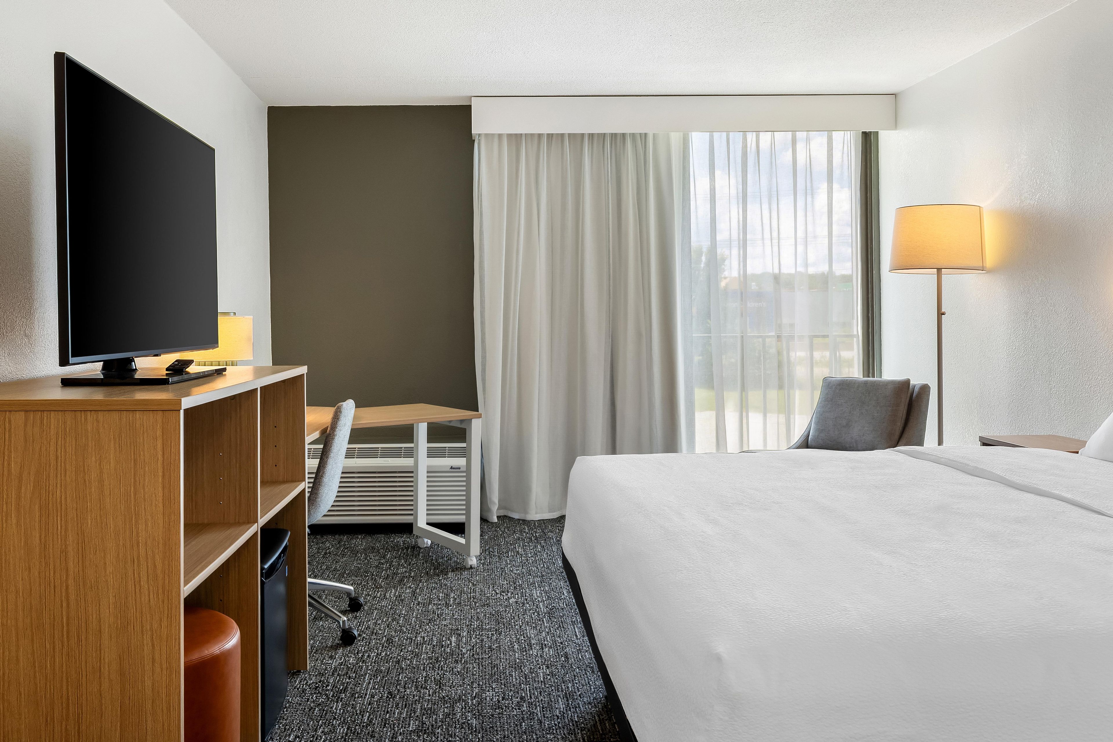 Une chambre d’hôtel équipée d’un lit, d’un bureau, d’une chaise, d’une télévision et d’une fenêtre avec des rideaux.