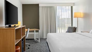 Une chambre d’hôtel équipée d’un lit, d’un bureau, d’une chaise, d’une télévision et d’une fenêtre avec des rideaux.