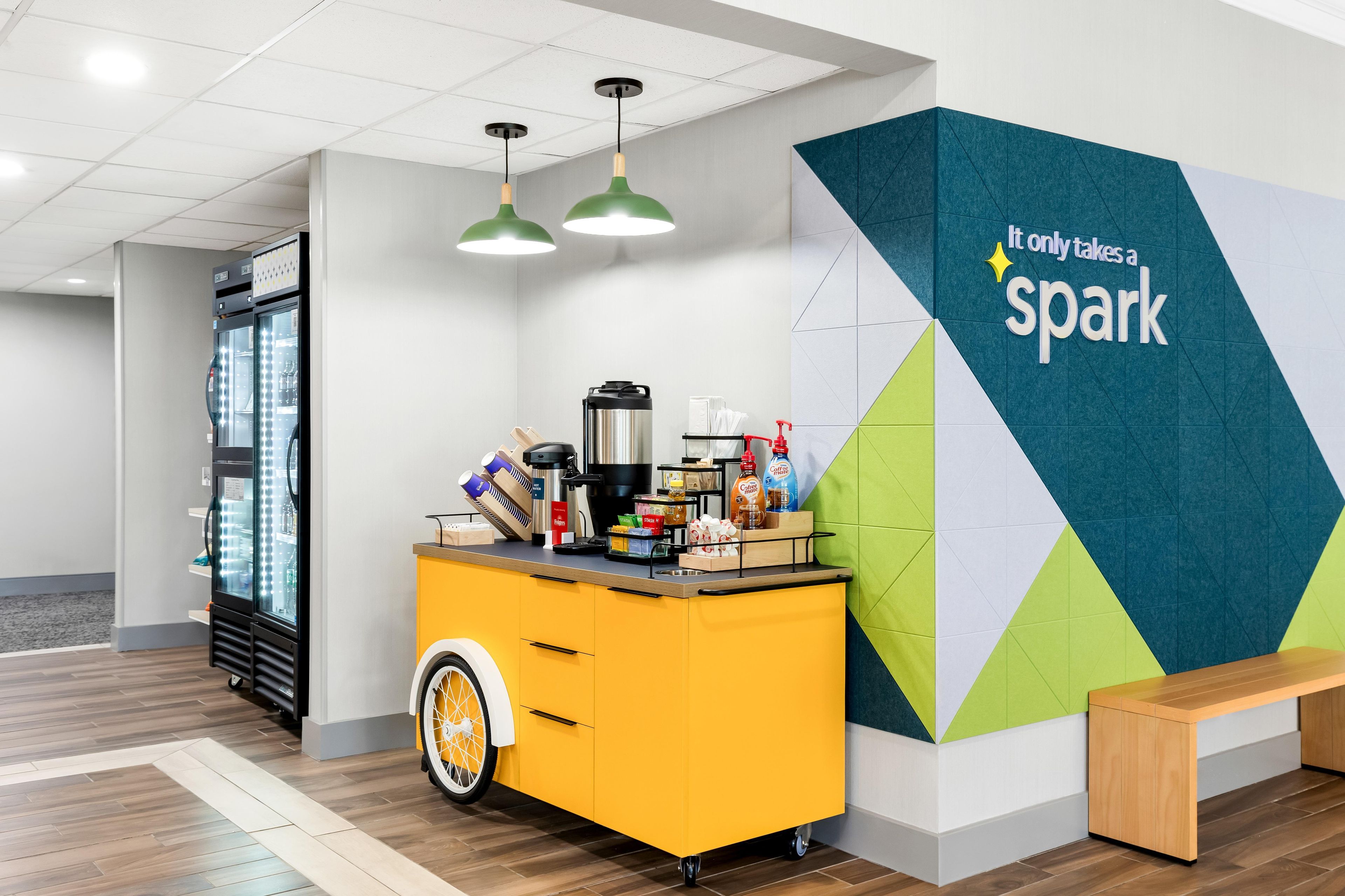 A modern kitchenette with a coffee station, a refrigerator, and a wall with a geometric design.