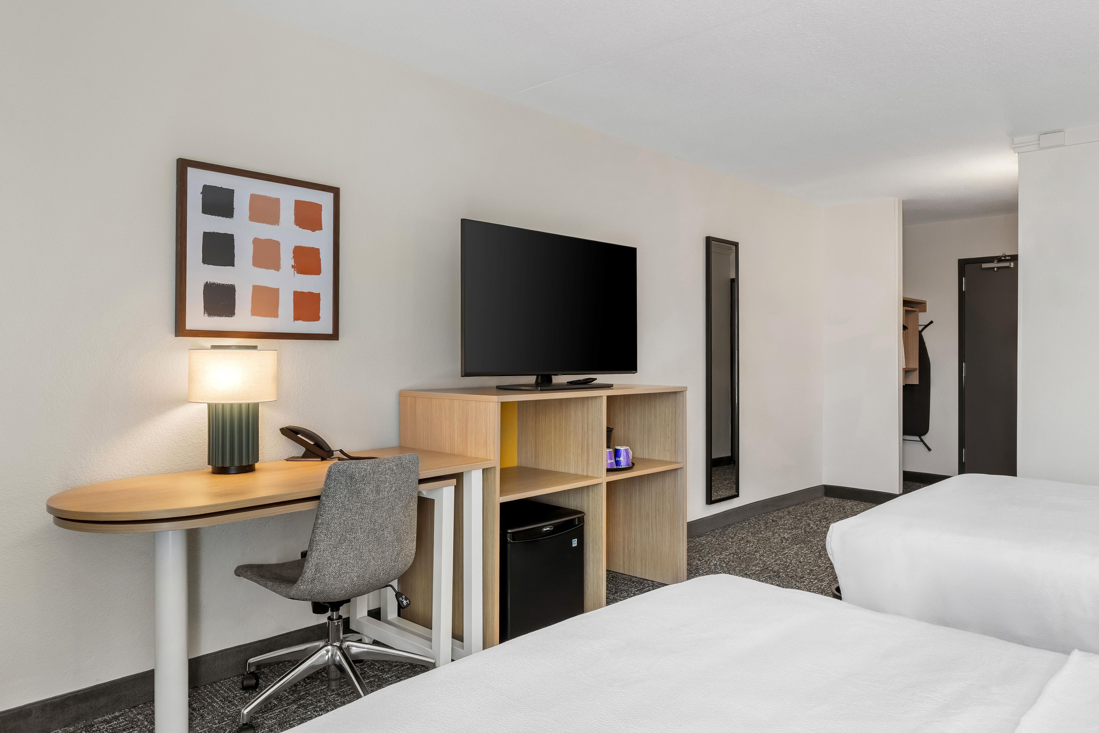 A hotel room with a desk, chair, television, and two beds.