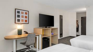A hotel room with a desk, chair, television, and two beds.