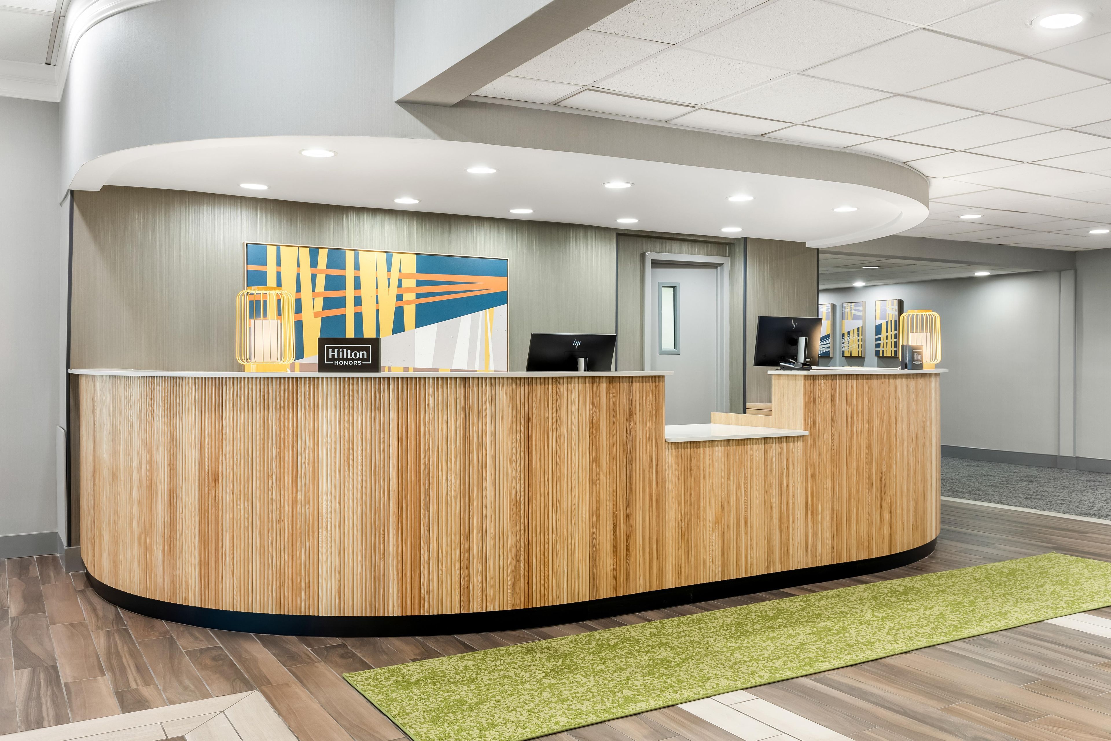A hotel reception desk with a wooden finish, a modern design, and a large abstract artwork above it.